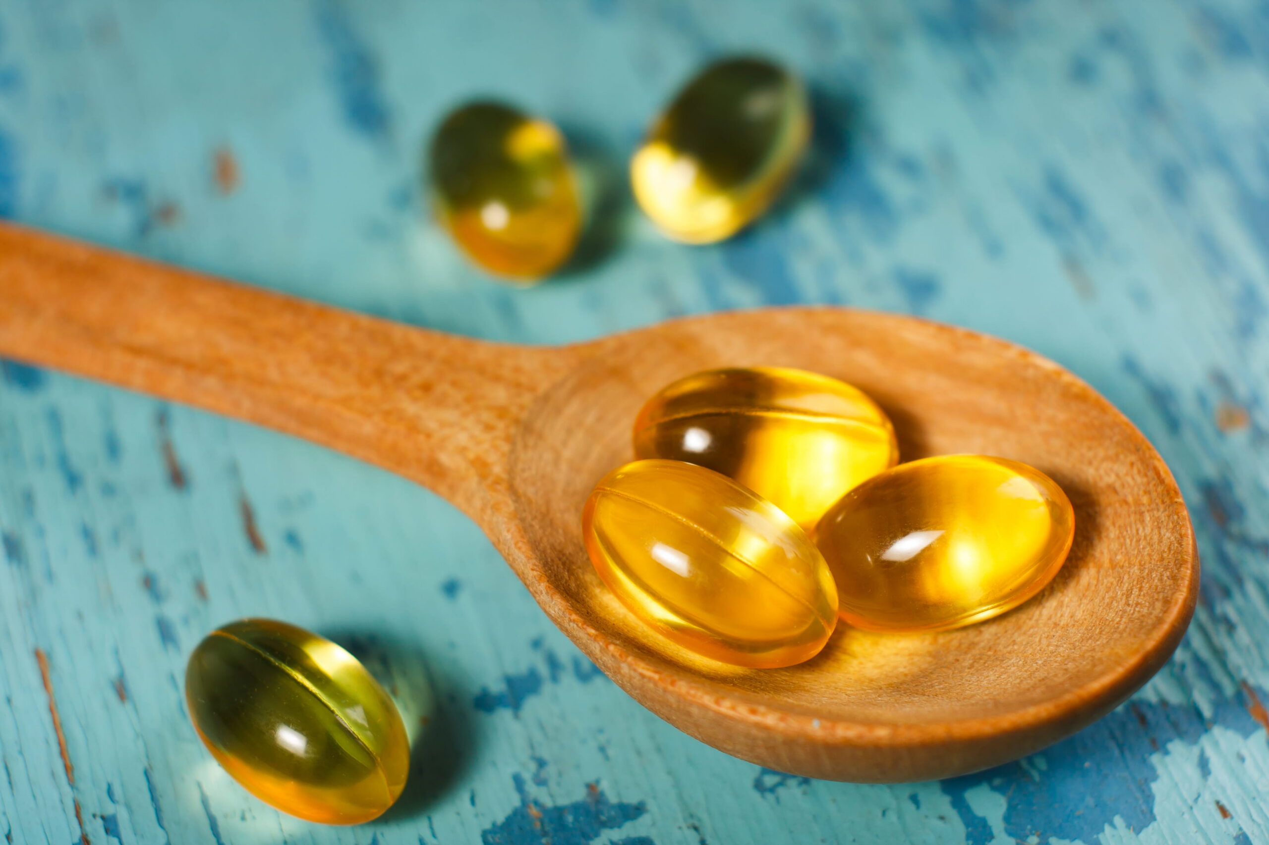 A wooden spoon holding liquid fish oil on a rustic blue table, representing daily omega-3 EPA and DHA supplementation.